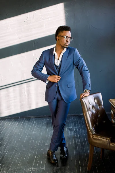 オフィスの椅子を彼の手を置くことでスタイリッシュなスーツ立ってで若い美しいアフリカ系アメリカ人の男 — ストック写真