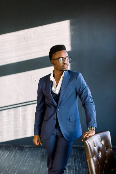 オフィスの椅子を彼の手を置くことでスタイリッシュなスーツ立ってで若い美しいアフリカ系アメリカ人の男 — ストック写真