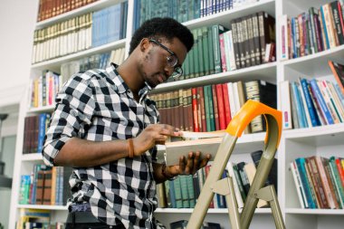 Rahat ve gülümseyerek adım merdiven yaslanmış iken arayan genç Afro-Amerikan öğrenci