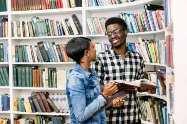 Güzel Afrikalı-Amerikalı öğrenciler kütüphanede çalışırlar. Kız gülümsüyor ve laptop ve çalışma, okuma kitapları ve çocuk dans müzik dinlerken.