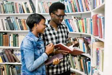 Güzel Afrikalı-Amerikalı öğrenciler kütüphanede çalışırlar. Kız gülümsüyor ve laptop ve çalışma, okuma kitapları ve çocuk dans müzik dinlerken.