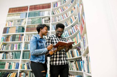 genç Afro-Amerikan öğrenciler kütüphane rafları arasında kitap okuma