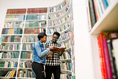 genç Afro-Amerikan öğrenciler kütüphane rafları arasında kitap okuma