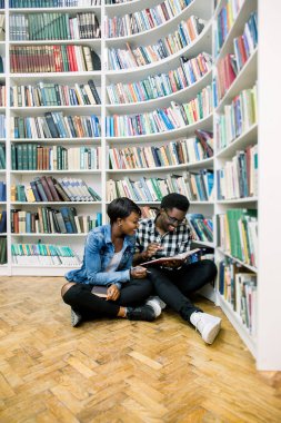 Güzel Afrikalı-Amerikalı öğrenciler kütüphanede çalışırlar. Kız gülümsüyor ve laptop ve çalışma, okuma kitapları ve çocuk dans müzik dinlerken.