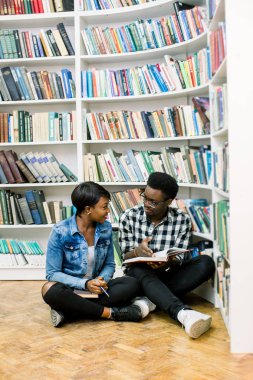 Güzel Afrikalı-Amerikalı öğrenciler kütüphanede çalışırlar. Kız gülümsüyor ve laptop ve çalışma, okuma kitapları ve çocuk dans müzik dinlerken.