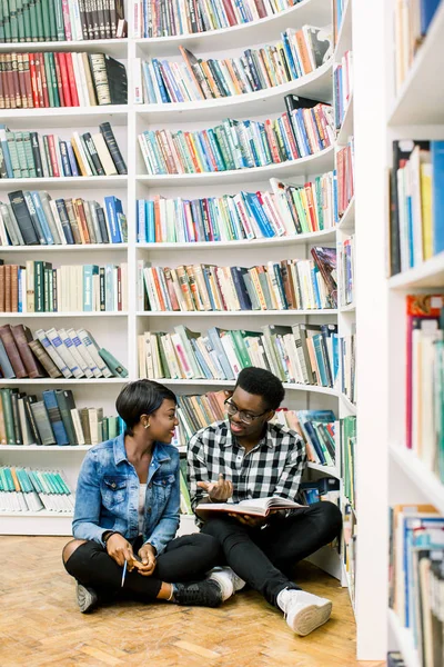 幸せな若いアフリカ系アメリカ人カップルは図書館の本棚で床に座って 笑顔と読書本ライブラリ — ストック写真