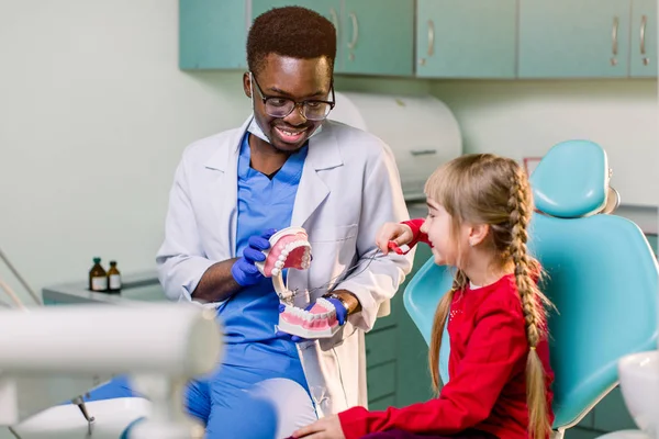 Niña Está Sentada Silla Dental Sonriendo Dentista Afroamericano Con Mandíbula —  Fotos de Stock