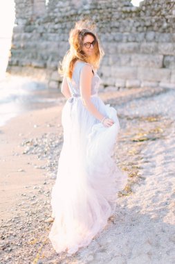 young beautiful woman in blue elegant dress walking near the lake Garda and fortress in Sirmione, Italy. Lovely walk in Sirmione