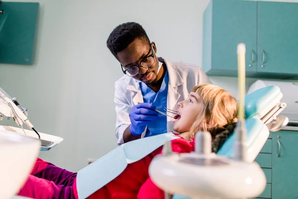 Teeth checkup at dentist\'s office. African-American dentist examining girls teeth in the dentists chair