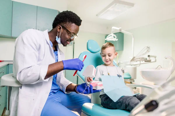 Dentista Preto Sorridente Feliz Diz Menino Caucasiano Como Escovar Dentes — Fotografia de Stock