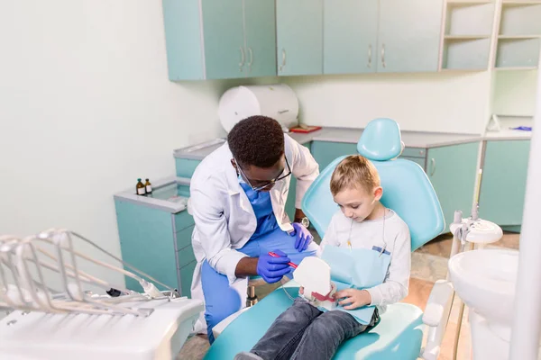 Pequeño Chico Caucásico Está Sentado Silla Dental Sonriendo Dentista Afroamericano —  Fotos de Stock