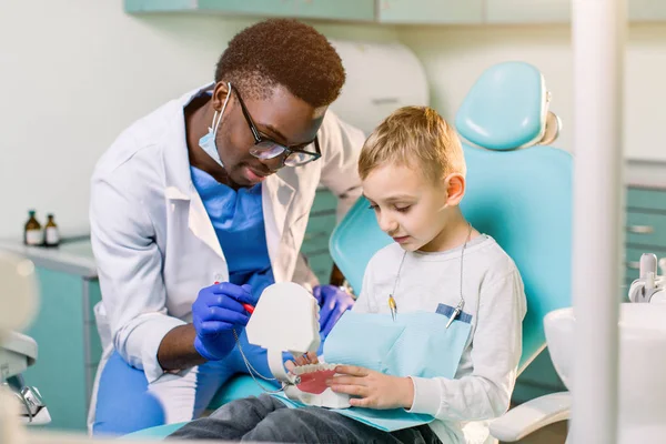 Pequeño Chico Caucásico Está Sentado Silla Dental Sonriendo Dentista Afroamericano —  Fotos de Stock