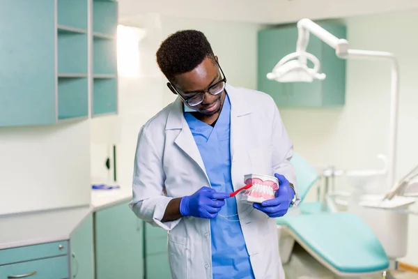 アフリカ系アメリカ人の歯科医は人工顎を使用して歯ブラシで歯を磨く方法を示しています — ストック写真
