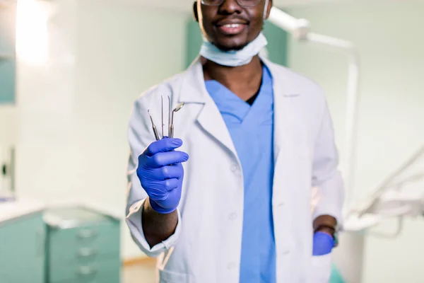 An African American dentist holds mirror and probe in his hands