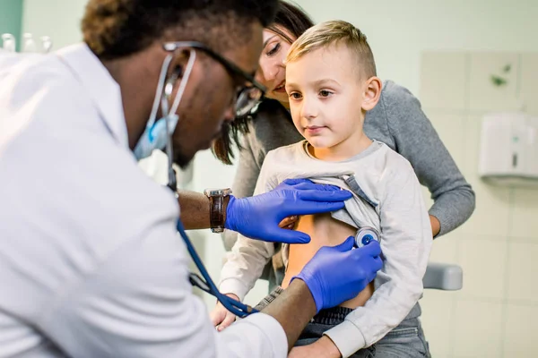 medicine, healthcare, pediatry and people concept - happy woman with her son and African American doctor with stethoscope at clinic