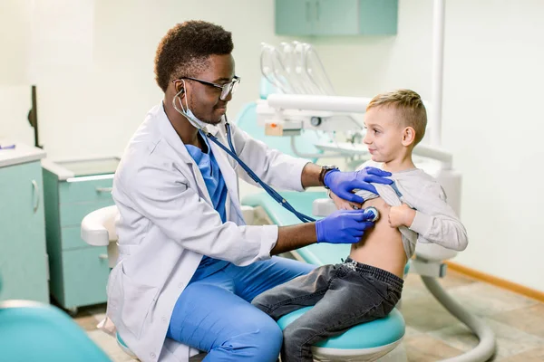 African American Doctor examining child by stethoscope. Happy child boy at the doctor\'s consultation in hospital. Medical exam at clinic by pediatrician. Pediatric, healthcare and people concept.