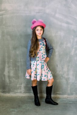 Koyu mavi elbise gri arka plan ayakta tarihinde eski bir ahşap dikiş makinesi üzerinde ellerini koyarak izole ifade içinde uzun esmer saçlı sevimli sevimli küçük kız