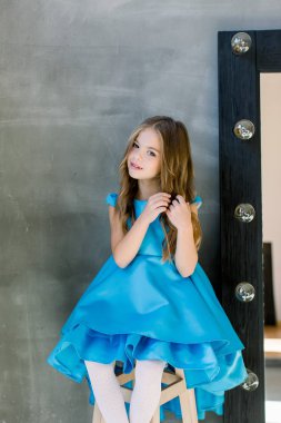 mavi bir elbise güzel mutlu küçük Bayan portresi taburede oturuyor ve saç dokunur