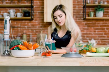 Onu mutfakta ayakta ve evde bir dizüstü bilgisayar üzerinde bir alışveriş listesi yazma mutlu güzel sarışın bir kadın. Sağlıklı gıda - sebze salatası. Diyet. Diyet kavramı. Sağlıklı bir yaşam tarzı. Evde yemek.