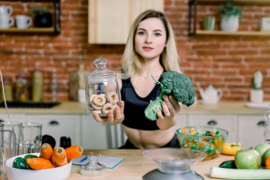 Genç kadın siyah spor giysileri tercih brokoli veya abur cubur, simit arasında. Sağlıklı temiz Detoks Beslenme kavramı. Vejetaryen, vegan ham kavramı. Kopya alanı.