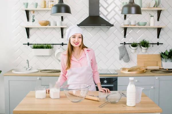 Beautiful young woman in chef hat looking at camera and smiling in the kitchen at home. Home cooking concept