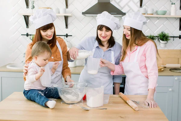 Happy family baking in the kitchen. Grandmother with her daughters and granddaughter preparing the dough, Granny pours milk from a bottle into a measuring glass