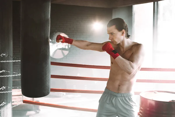 Rozzlobený boxer stojící v boxerské póze poblíž boxovací pytel na černém pozadí s kouřem — Stock fotografie