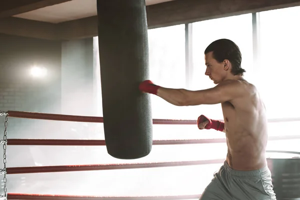 Wütender Boxer steht in Boxerpose neben Boxsack auf schwarz mit Rauch — Stockfoto