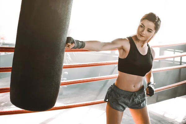 Mulher bonita e confiante boxeador atlético saco de perfuração durante a preparação de treinamento para a batalha . — Fotografia de Stock