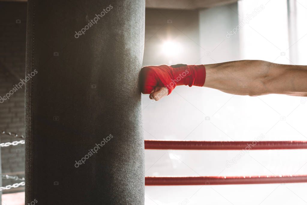 Hand of boxer and punching bag over dark background
