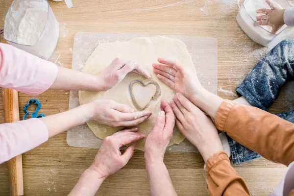 Concetto di cucina e casa - primo piano di mani femminili che fanno biscotti da pasta fresca a casa. Le mani di tre donne tengono il biscotto in forma di cuore — Foto Stock