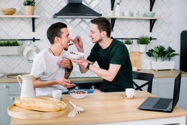 Başka bir gülümseme ile kahvaltı sırasında arayan iki mutlu genç homoseksüel erkekler. Adam ortağı besleme