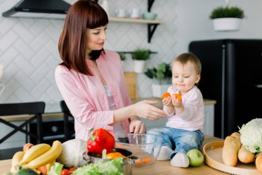 Genç anne ve sağlıklı gıda hazırlama ve having fun sevimli küçük bebek kız gülümseyerek, bebek tutan ve havuç yiyor