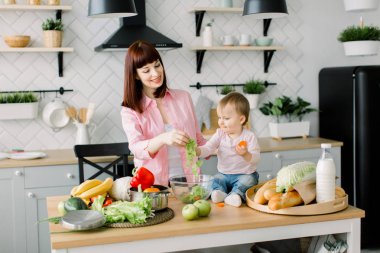 Anne ve küçük kızı yemek masasında hazırlamak bir sabah kahvaltı taze sebze. Anne ve çocuk cam kaseye koyarak yeşil marul birlikte, taze salata hazırlık