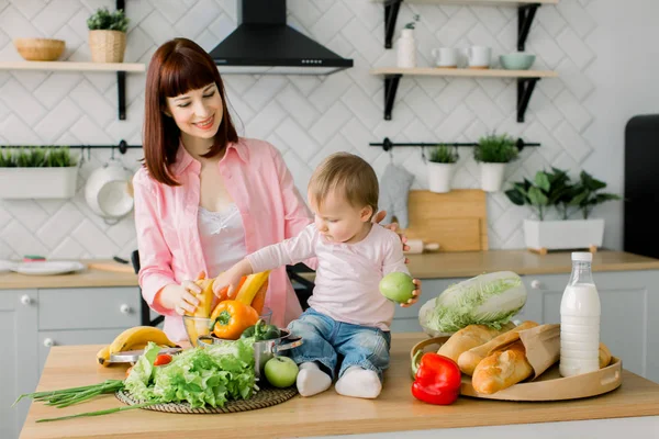 Az egészséges táplálkozás. Boldog család anya és kis baba lány előkészíti a konyhában zöldségsaláta — Stock Fotó