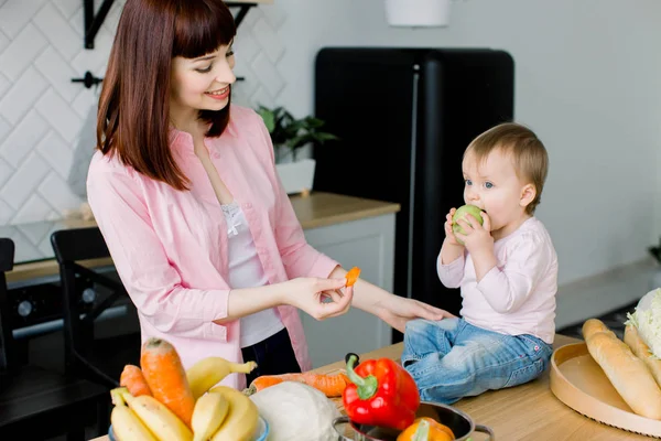 Boldog anya, és szórakozás közben együtt főzés, a konyha, kislány baba. Evés sárgarépa és zöld alma evés baba anya. Egészséges életmód, a friss élelmiszer-, családi főzés — Stock Fotó