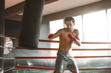 Koyu renk spor salonunda boksör eğitimi. Genç boksör kum torbası eğitimi alıyor. Büyük dövüş için erkek boksör. Boksör kum torbasına vurdu.