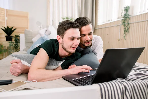 Tecnología moderna. bastante joven gay pareja usando laptop mientras posando en cama y pasando tiempo juntos —  Fotos de Stock