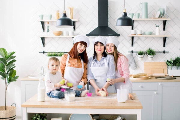 Счастливая семья на кухне. Молодая женщина и ее сестра, женщина среднего возраста и маленькая милая дочь приготовления кексов на День матери, случайный образ жизни фотосерии в реальной жизни интерьера
