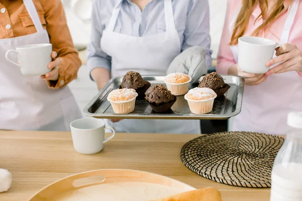 Cupcake, muffins, baking together - three women hold freshly baked chocolate and vanilla cupcakes on baking tray. Family cooking, Mothers Day concept