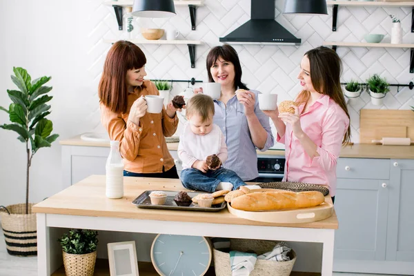 Vonzó a fiatal nők, középső idősebb nő és a kis aranyos lány a konyhában a főzés. Szerető család eszik a muffin, a konyhában és a kávéfogyasztás — Stock Fotó