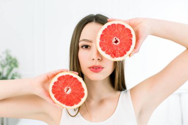 Uzun saçlı, kusursuz cilt ve mükemmel makyaj, güzel genç gülümseyen kadın greyfurt parçaları üzerinde beyaz izole holding