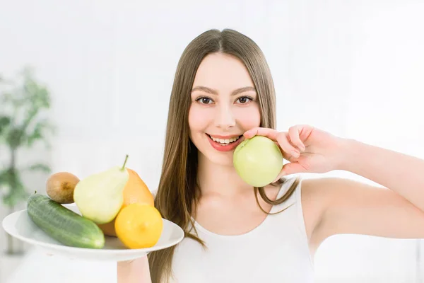 Sonrisa sana, hermosa, linda chica sonriendo. Retrato de una niña con plato de frutas en una mano y una manzana en otra . — Foto de Stock