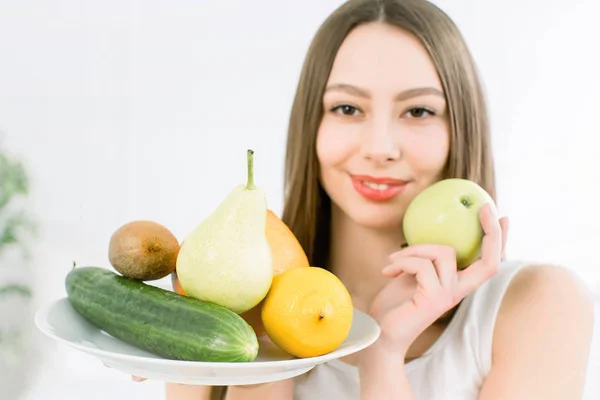 Atractiva joven mujer caucásica sonriente sosteniendo un plato con verduras y frutas verdes amarillas en el fondo claro. Saludable, belleza, buena comida productos vegetarianos . — Foto de Stock
