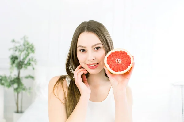 Szépség portréja vonzó egészséges nő állandó elszigetelt át világos háttér, pózol a fele lédús grapefruit közelében az arcát, és nézi a kamera — Stock Fotó
