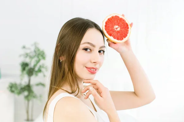 Belleza mujer sonriente con pomelo cítrico naranja con cuerpo de piel sana posando sobre el fondo claro. Atractiva vitamina fresca. Sesión de estudio . —  Fotos de Stock