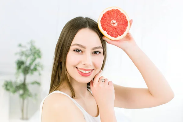 Belleza mujer sonriente con pomelo cítrico naranja con cuerpo de piel sana posando sobre el fondo claro. Atractiva vitamina fresca. Sesión de estudio . — Foto de Stock