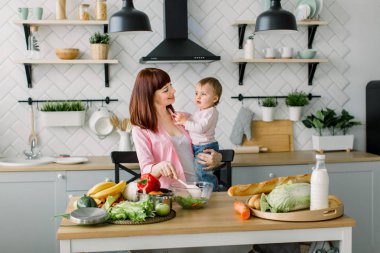 Pembe gömlekli neşeli güzel annem mutfakta, taze bir sebze salatası evde küçük şirin kızı tutan hazırlanıyor. Anne ve kızı, sağlıklı gıda kavramı