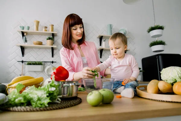 Mothers Day, food, healthy eating, cooking and family concept - happy mother and little baby girl preparing salad with fresh lettuce at home kitchen