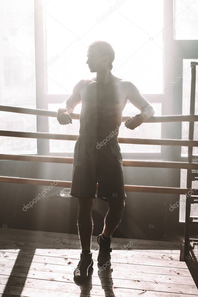 Portrait of sportive boxer wearing boxing bandages on hands while having break after workout in gym